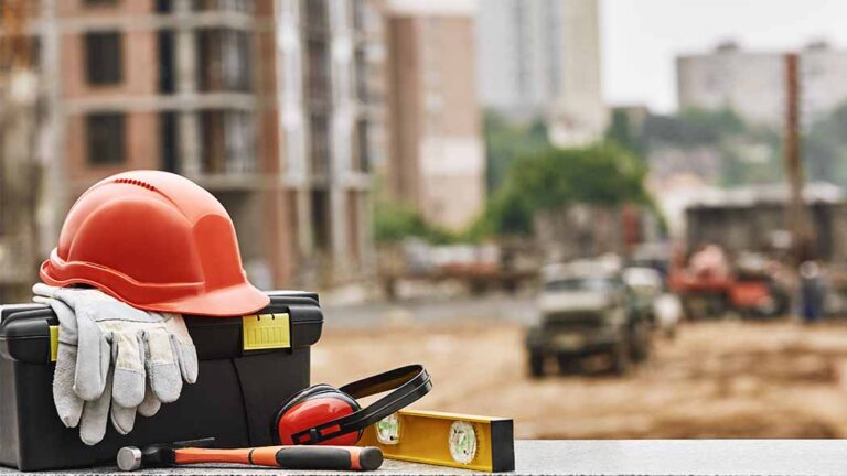 PPE laid out by a contractor with a backdrop of a construction site, with the equipment in focus as health and safety of contractors is of critical importance.