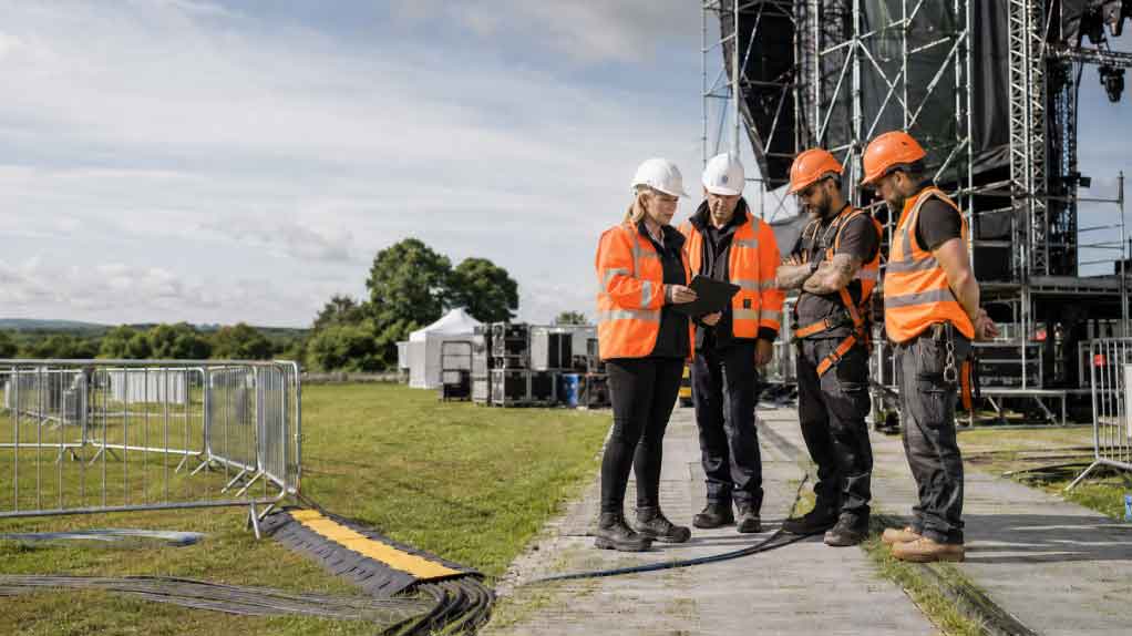 Contractors wearing orange high-vis during an HSA summer inspection campaign in Ireland, reviewing safety compliance, hazards, and controls at an outdoor event worksite.