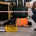 Workplace accident scene in an industrial warehouse with workers in orange high-vis, highlighting the importance of safety programme compliance and fatality prevention.