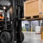 Forklift operator carefully lifting a crate in a warehouse, representing safe load-handling practices highlighted after a crate falling from forklift incident.